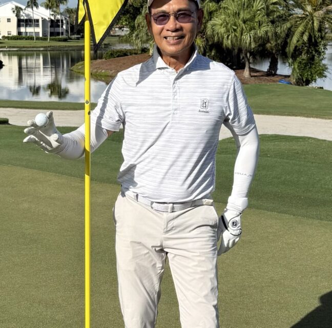 Wen Wu on the ninth green holding the flagstick and his ball after a hole-in-one