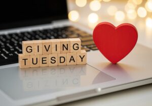 Wooden letter blocks spelling Giving Tuesday beside a red heart on a laptop