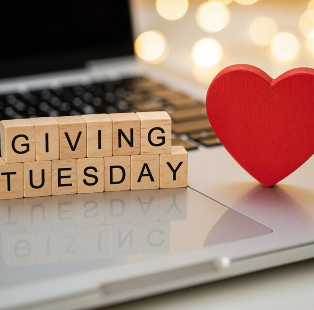 Wooden letter blocks spelling Giving Tuesday beside a red heart on a laptop
